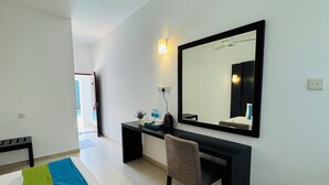 A hotel room with a desk, chair, and a large mirror. There is a small table with a plant and a water bottle on the desk. The room has white walls and a tiled floor. - Seaport Negombo (Negombo)