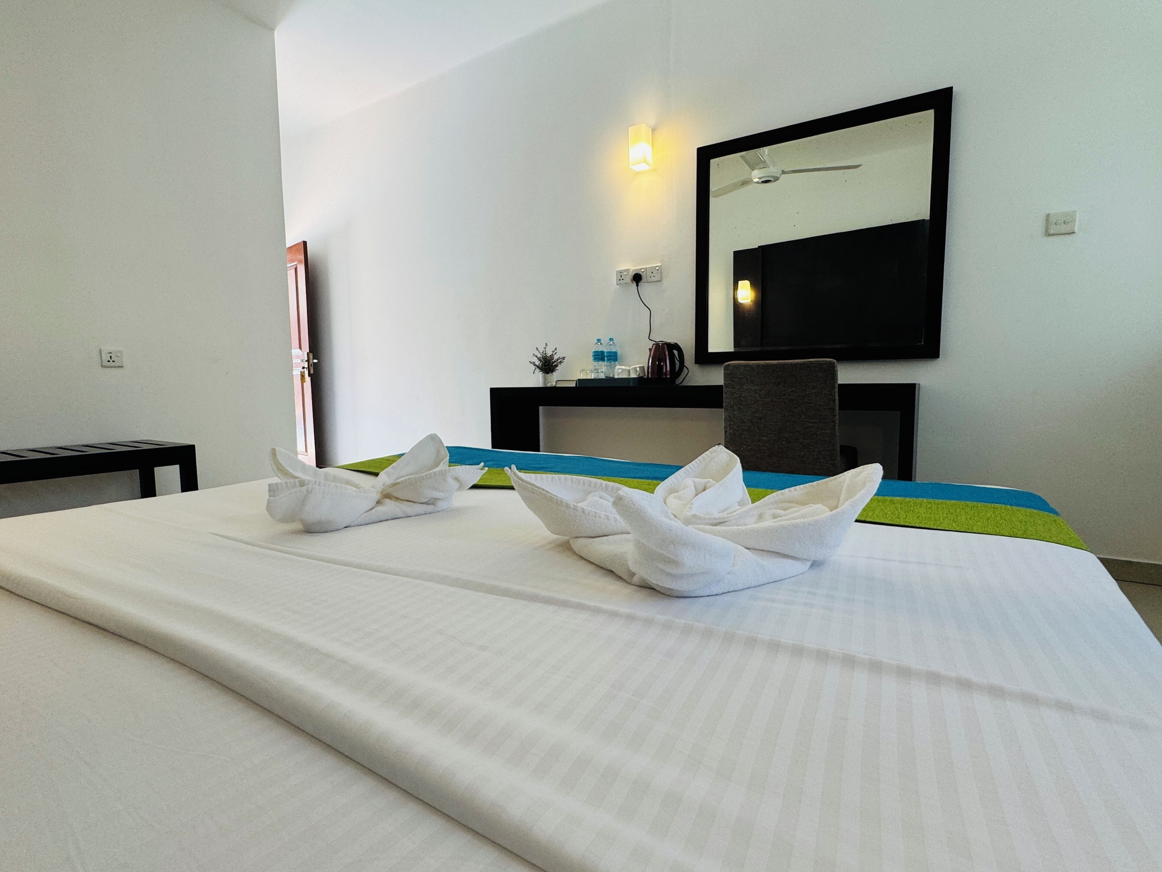 A hotel room with a bed, a desk, a chair, a mirror, and a wall-mounted light.