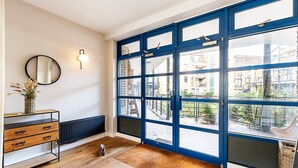 Ein Zimmer mit großem Fenster, Heizkörper, Holzkommode, rundem Spiegel und einem kleinen Hund.