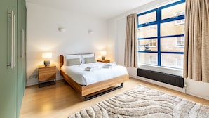 Ein modernes Schlafzimmer mit einem hölzernen Bett, zwei Nachttischen mit Lampen, einem großen Fenster mit Vorhängen und einer Heizung.
