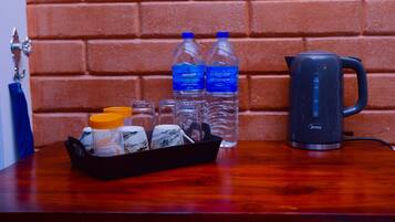 A table with a black tray containing a bottle of water, a thermos, and a mug. There are two bottles of water and a kettle on the table.