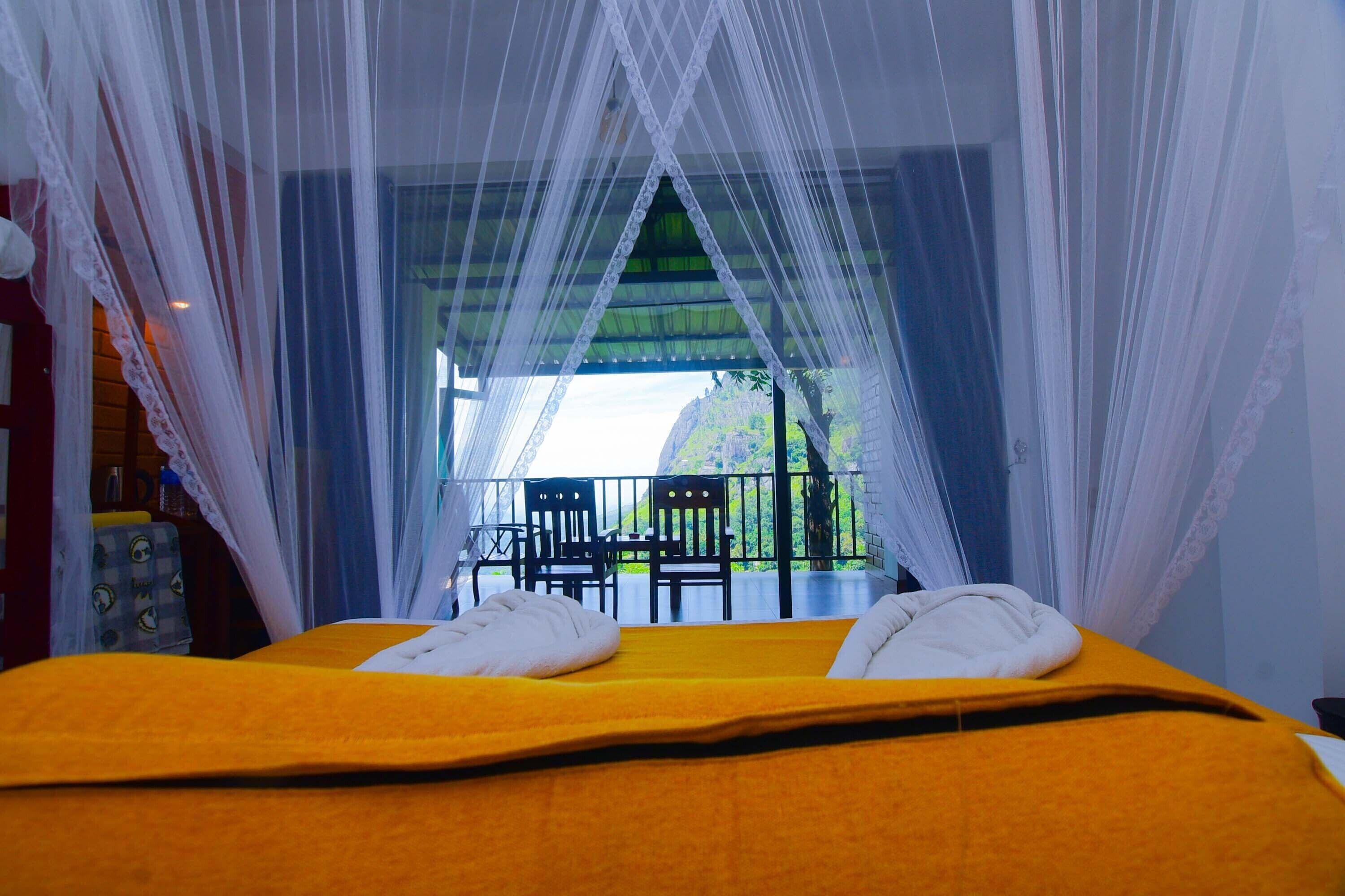 Una cama con una colcha amarilla y almohadas blancas, un dosel y vistas a un área exterior con sillas y una mesa.