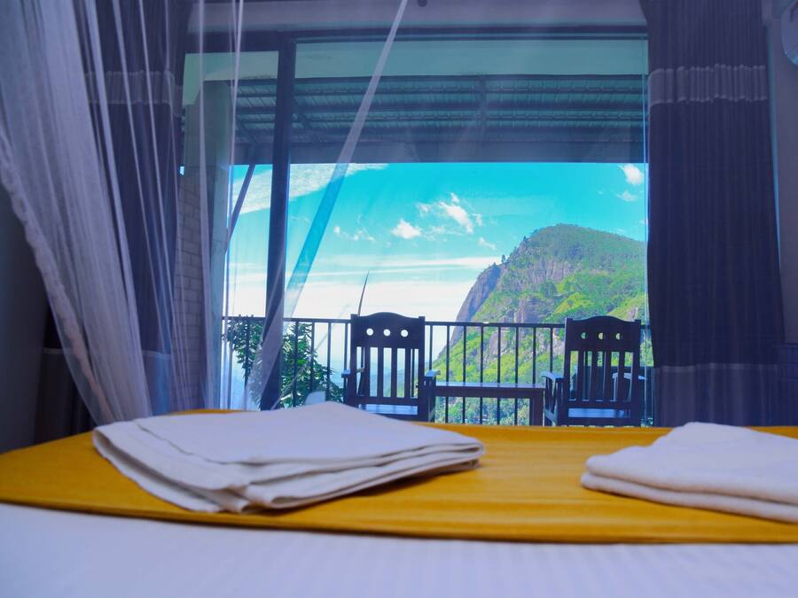 Habitació d'hotel amb un llit, una taula i cadires, i un finestral gran que ofereix vistes a un paisatge de muntanya.