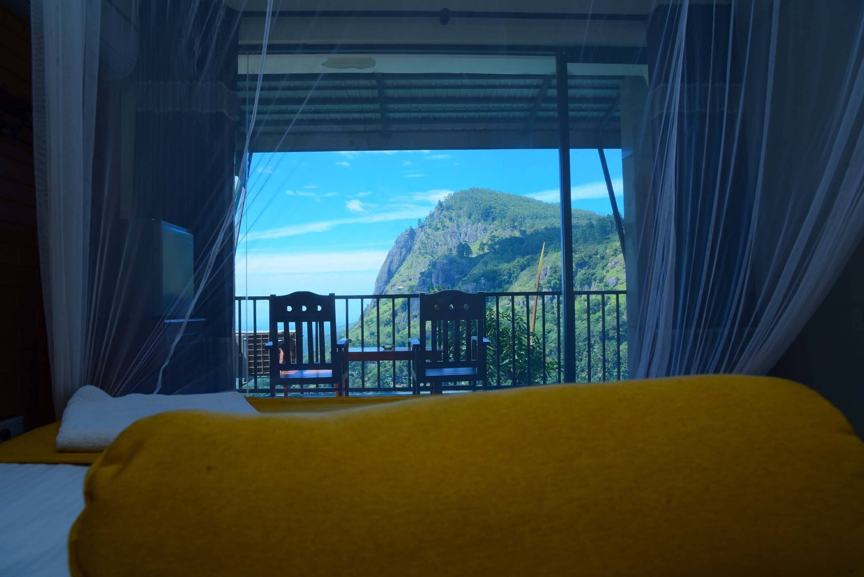 Ein Zimmer mit Bett, einem Balkon mit Stühlen und Blick auf einen Berg.