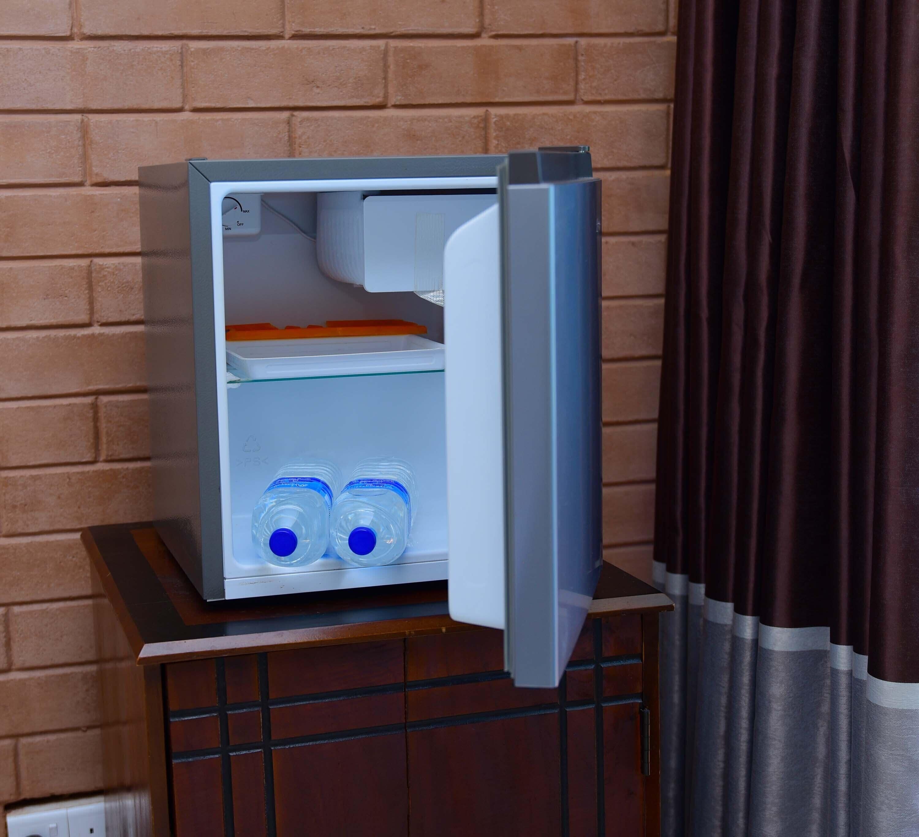 A small refrigerator with two water bottles inside, placed on a wooden cabinet against a brick wall.