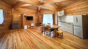 A wooden cabin interior with a dining area, kitchen, and a small seating area. - Asahi Prime Resort Cottages (Asahi)