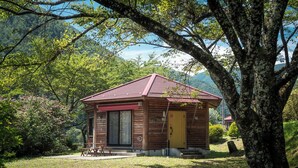A small wooden cabin with a red roof, a door, and a window, surrounded by trees and a grassy area. - Asahi Prime Resort Cottages (Asahi)