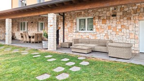 Une terrasse extérieure couverte, avec des murs en pierre, des meubles en osier et un chemin en pierre.