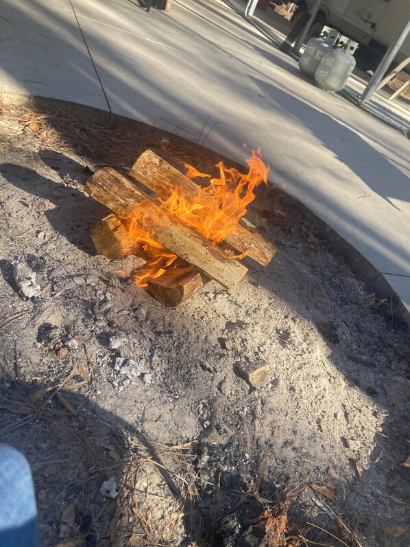Fuego ardiendo sobre una superficie de concreto, con leña y una estructura metálica al fondo.