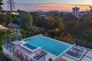 Una piscina rettangolare con piattaforma di tuffo, circondata dal verde e con vista sulla città.