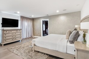 Una camera da letto moderna con un letto grande, una cassettiera, un televisore e un cabina armadio.
