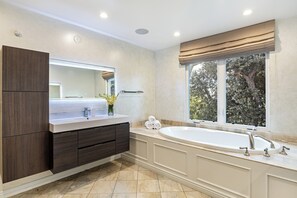 Un bagno moderno con una vasca da bagno ampia, un doppio lavabo con specchio e una finestra vista alberi.