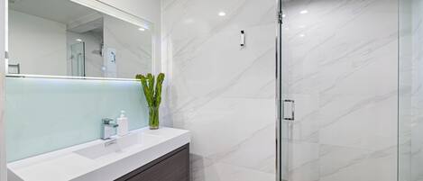 A modern bathroom with a white vanity, a glass shower enclosure, and marble walls.