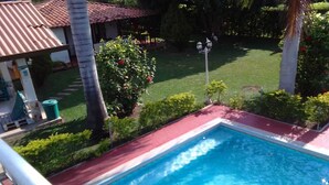 Une piscine bordée de rouge, entourée de verdure et un bâtiment avec un toit rouge.