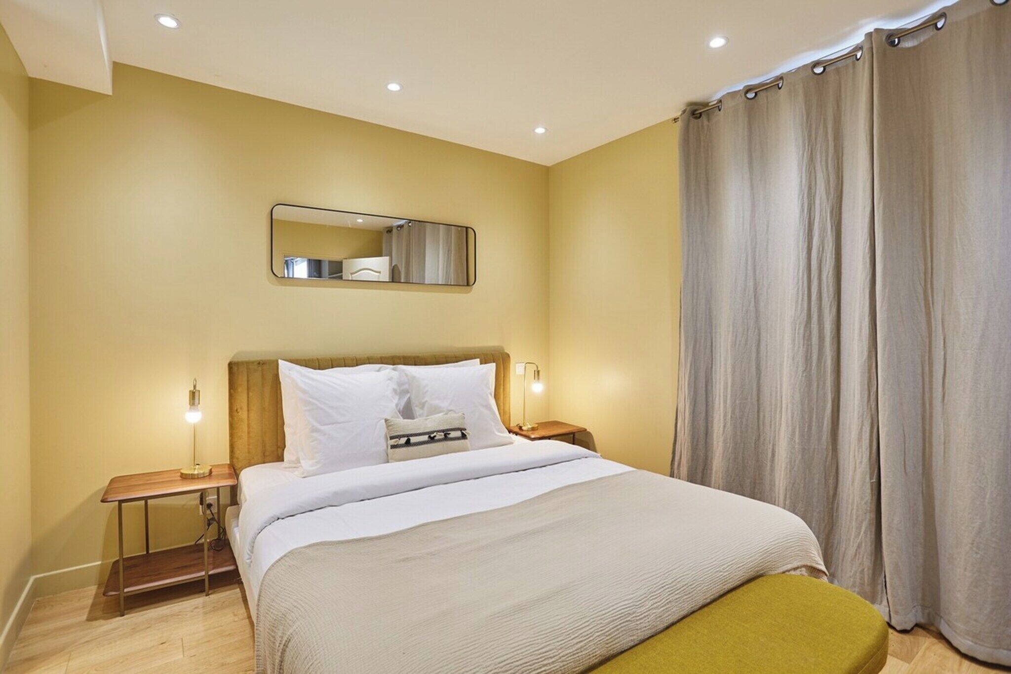 Une chambre d’hôtel avec un lit, des tables de chevet, un miroir et un rideau.