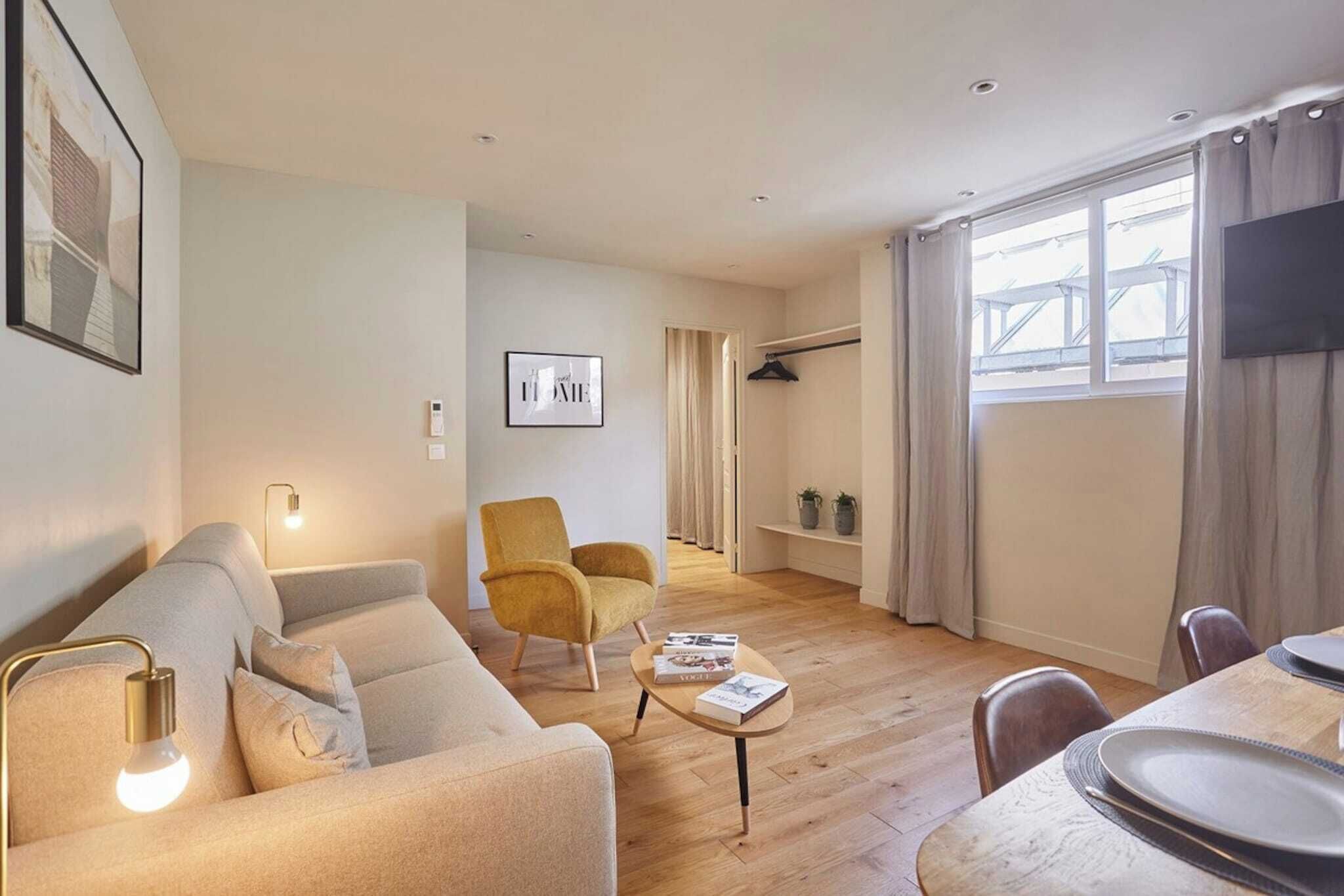 Un salon moderne comprenant un canapé, un fauteuil et une table basse, un coin repas avec une table et des chaises, et une grande fenêtre avec des rideaux.