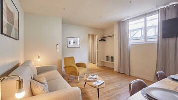 Un salon moderne comprenant un canapé, un fauteuil et une table basse, un coin repas avec une table et des chaises, et une grande fenêtre avec des rideaux.