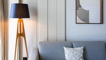 Una habitación con un sofá gris, un cojín estampado, una lámpara de pie con pantalla oscura y una obra de arte abstracta en la pared.