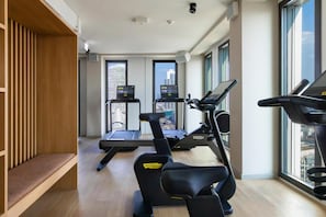 A modern gym with two treadmills, one elliptical, and a bench. - ATLANTIC Hotel Frankfurt - New opening (Frankfurt)