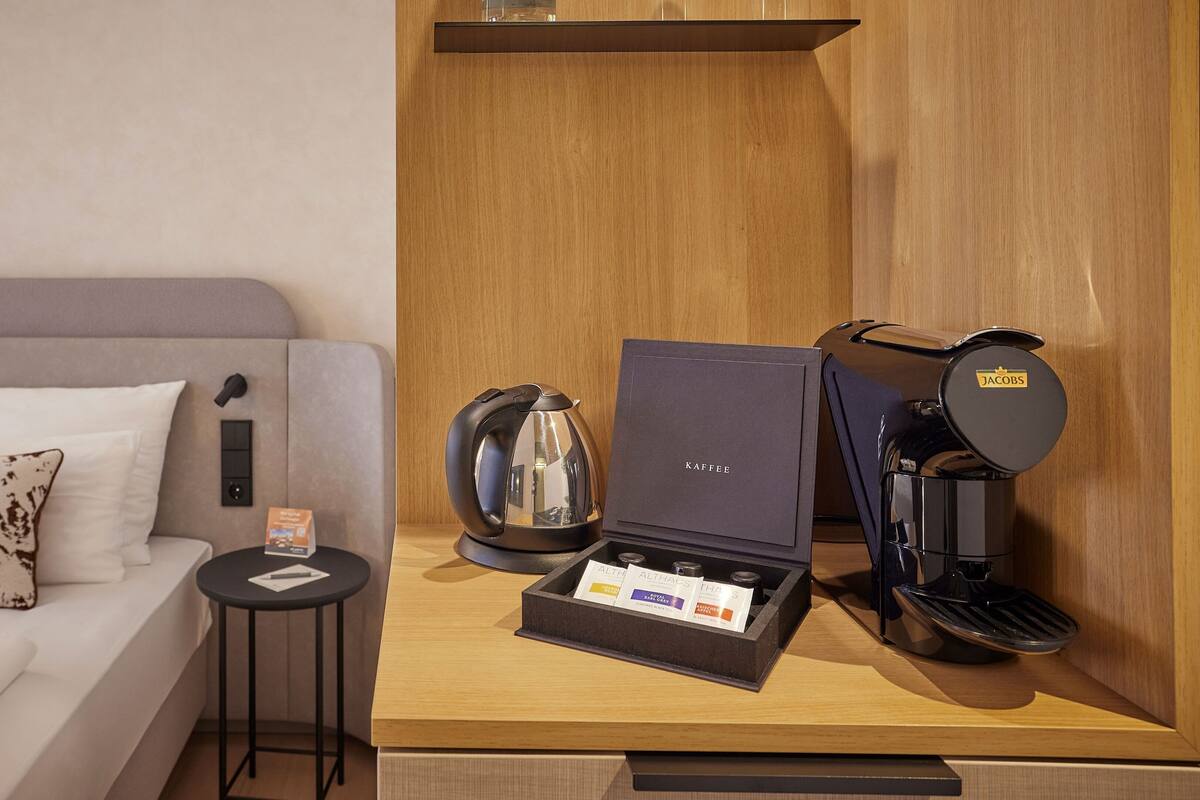 Ein Hotelzimmer mit einem Bett, einer Kaffeemaschine, einem Wasserkocher und einer Kapselkaffeeverpackung.