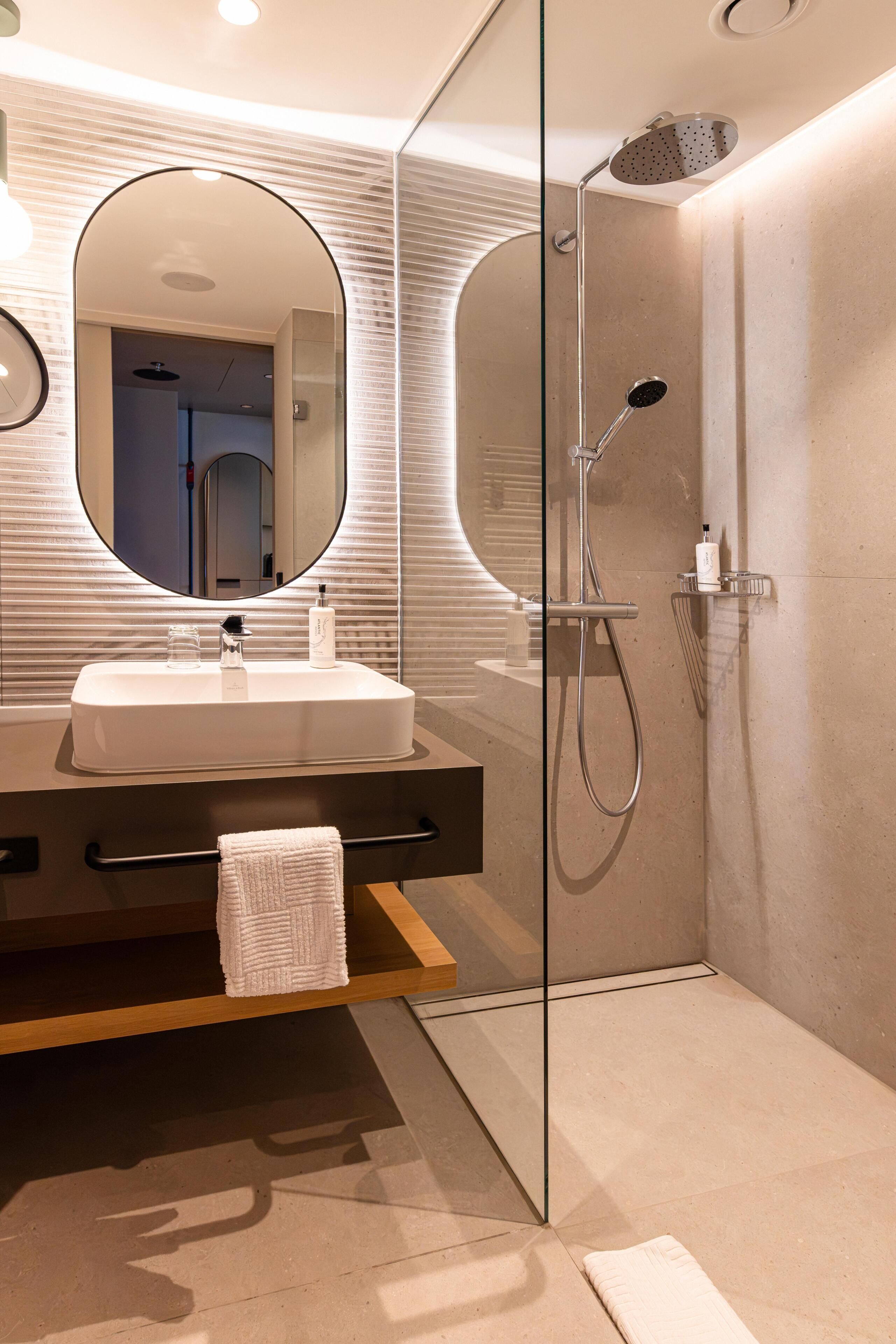 A modern bathroom with a glass-enclosed shower, a large mirror, and a wooden vanity with a towel.