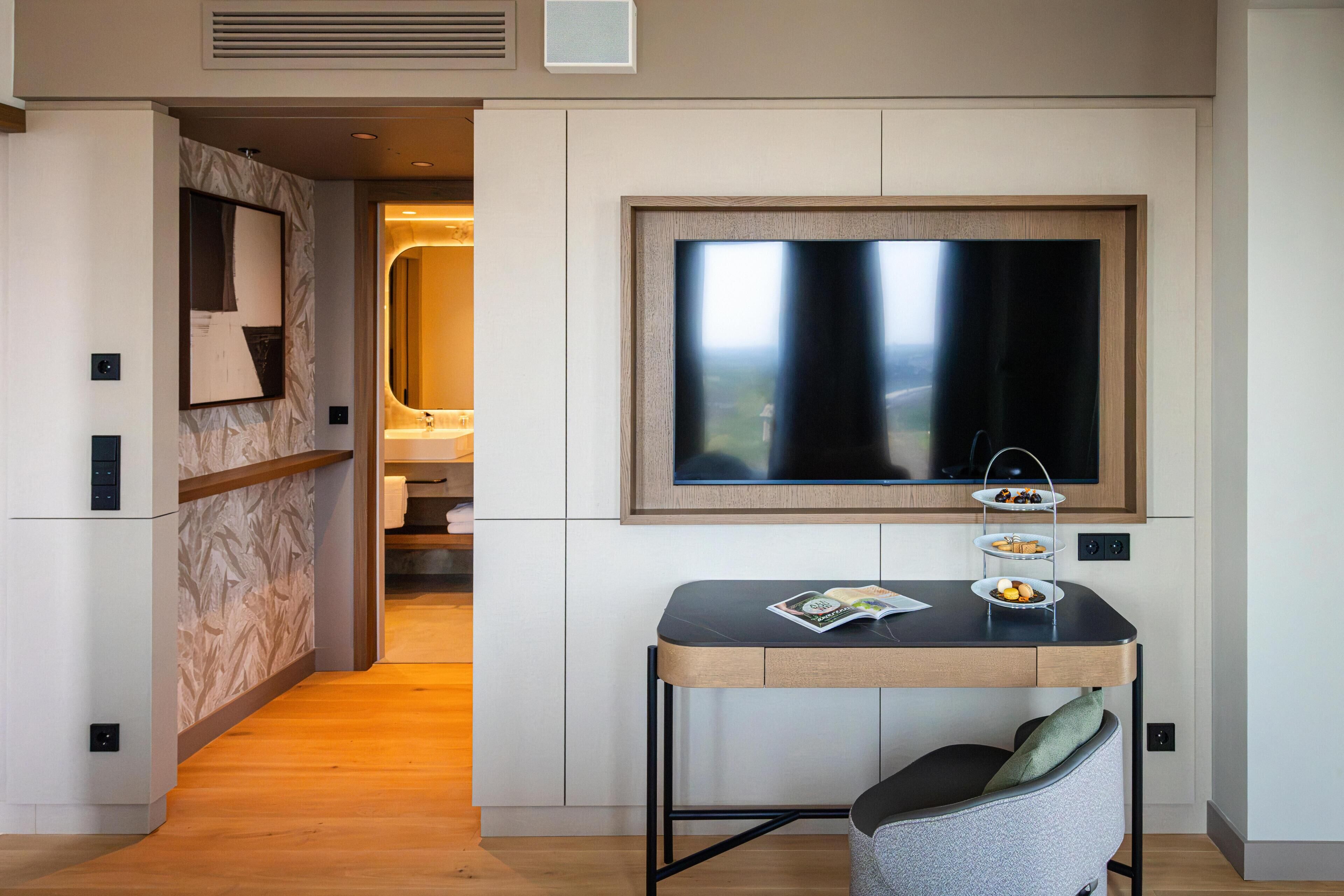 A modern hotel room with a large window, a small dining table with a magazine, and a cozy seating area.