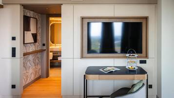 A modern hotel room with a large window, a small dining table with a magazine, and a cozy seating area.