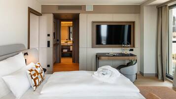 A hotel room with a large bed, a desk with a flat-screen TV, a bathroom with a mirror, and a view of the city through the window.