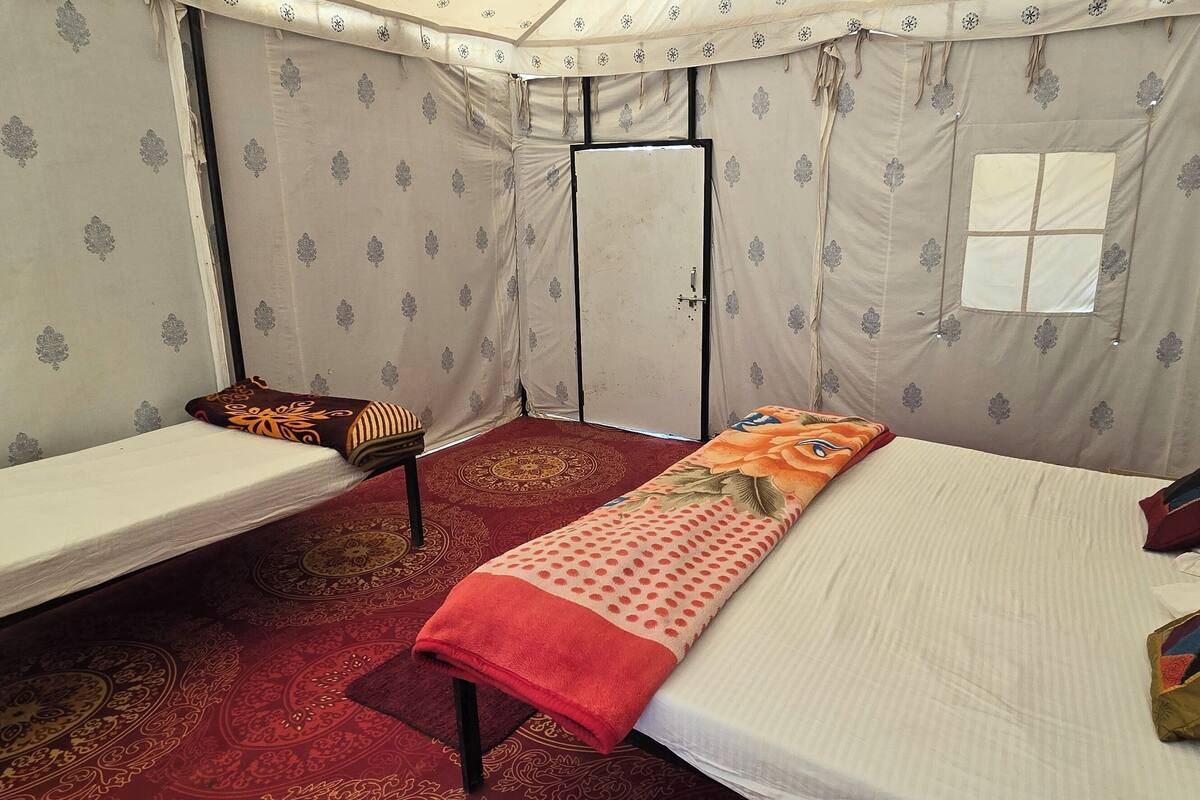 A small, enclosed room with two single beds, a window, and patterned curtains.