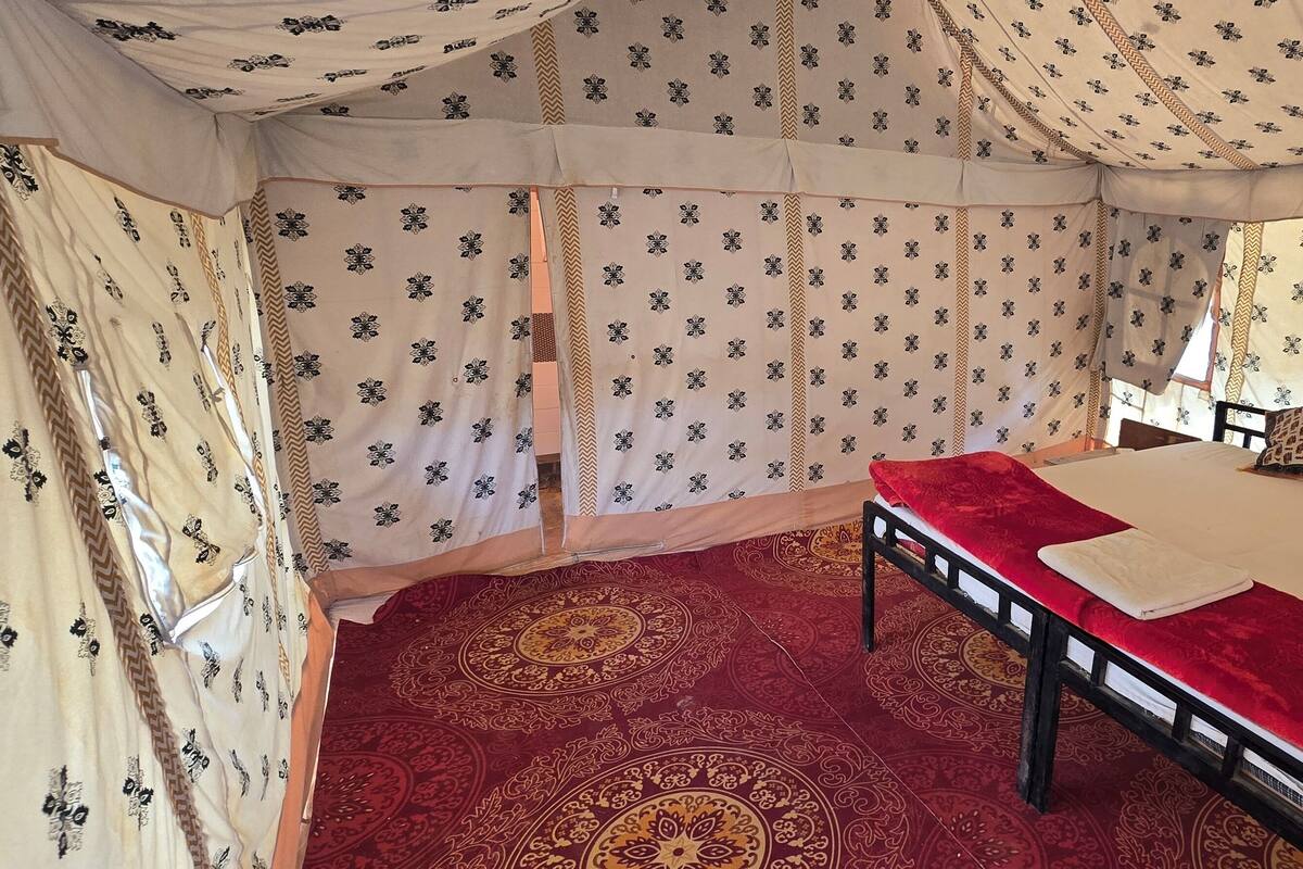 A tent with a bed, a red carpet, and patterned curtains.
