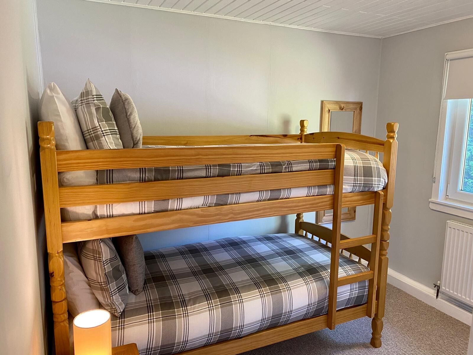 A bunk bed with plaid bedding, a bedside lamp, and a window with blinds.