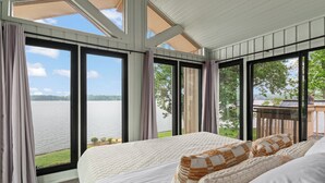 Una camera da letto con un letto grande, vista su un lago e un balcone con pavimento in legno.