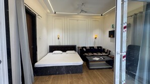 Una camera d'albergo con un letto, un divano, un tavolino e una ventola a soffitto.