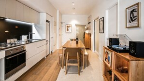 A modern kitchen with a dining area, featuring a wooden table, chairs, and a built-in sound system. - Super King Beds, Vinyl + Pool | CBD Luxury (Melbourne)