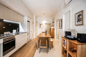 A modern kitchen with a dining area, featuring a wooden table, chairs, and a built-in sound system. - Super King Beds, Vinyl + Pool | CBD Luxury (Melbourne)