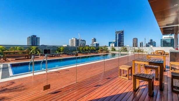 A rooftop pool area with a clear view of the city skyline, wooden deck, and lounge chairs. - Super King Beds, Vinyl + Pool | CBD Luxury (Melbourne)