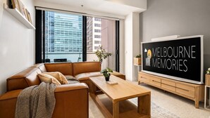 A modern living room with a leather sofa, a wooden coffee table, and a large flat-screen TV displaying 'Melbourne Memories'. - Super King Beds, Vinyl + Pool | CBD Luxury (Melbourne)