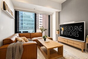 A modern living room with a leather sofa, a wooden coffee table, and a large flat-screen TV displaying 'Melbourne Memories'. - Super King Beds, Vinyl + Pool | CBD Luxury (Melbourne)