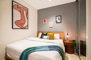 Une chambre à coucher avec un lit, une table de chevet, une lampe et des œuvres d’art murales.