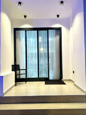 Una habitación moderna con una puerta corrediza de vidrio, una silla negra y una alfombra pequeña.