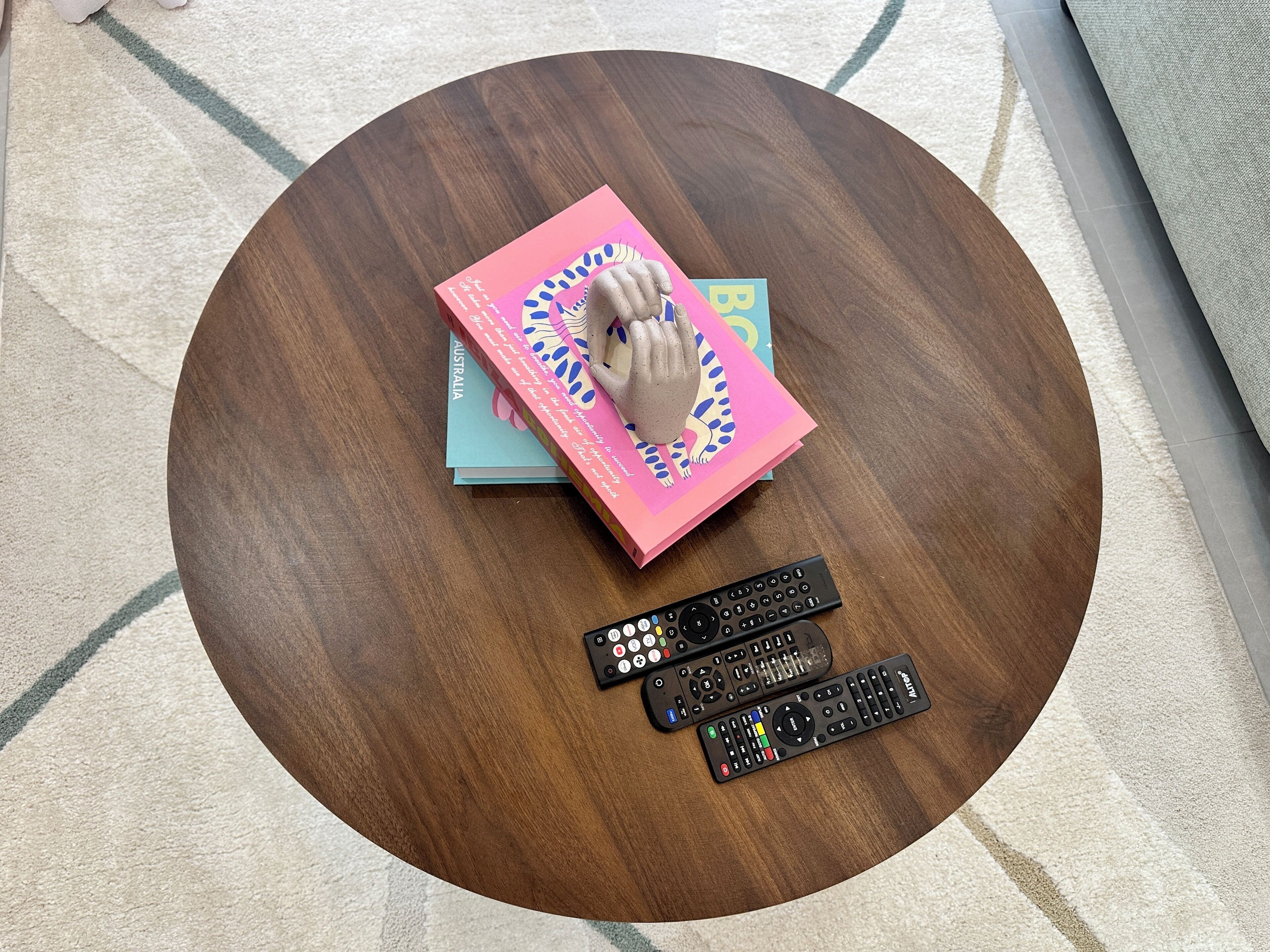 Una mesa de madera redonda con una pila de libros y dos controles remotos.