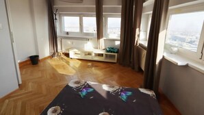 A hotel room with a bed, a window with a view of the city, a radiator, and a small seating area. - Fantastic Inn Warsaw - CH35 (Warsaw)