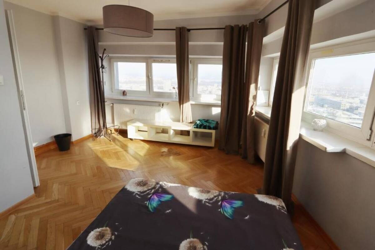 A hotel room with a bed, a window with a view of the city, a radiator, and a small seating area.