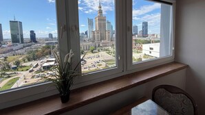 A room with a large window overlooking a cityscape, a wooden bench, and a potted plant. - Fantastic Inn Warsaw - CH35 (Warsaw)