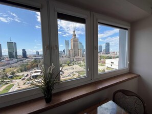 A room with a large window overlooking a cityscape, a wooden bench, and a potted plant. - Fantastic Inn Warsaw - CH35 (Warsaw)