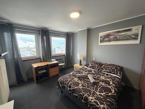 A hotel room with a bed, a desk, a chair, a lamp, and a city view. - Fantastic Inn Warsaw - CH35 (Warsaw)