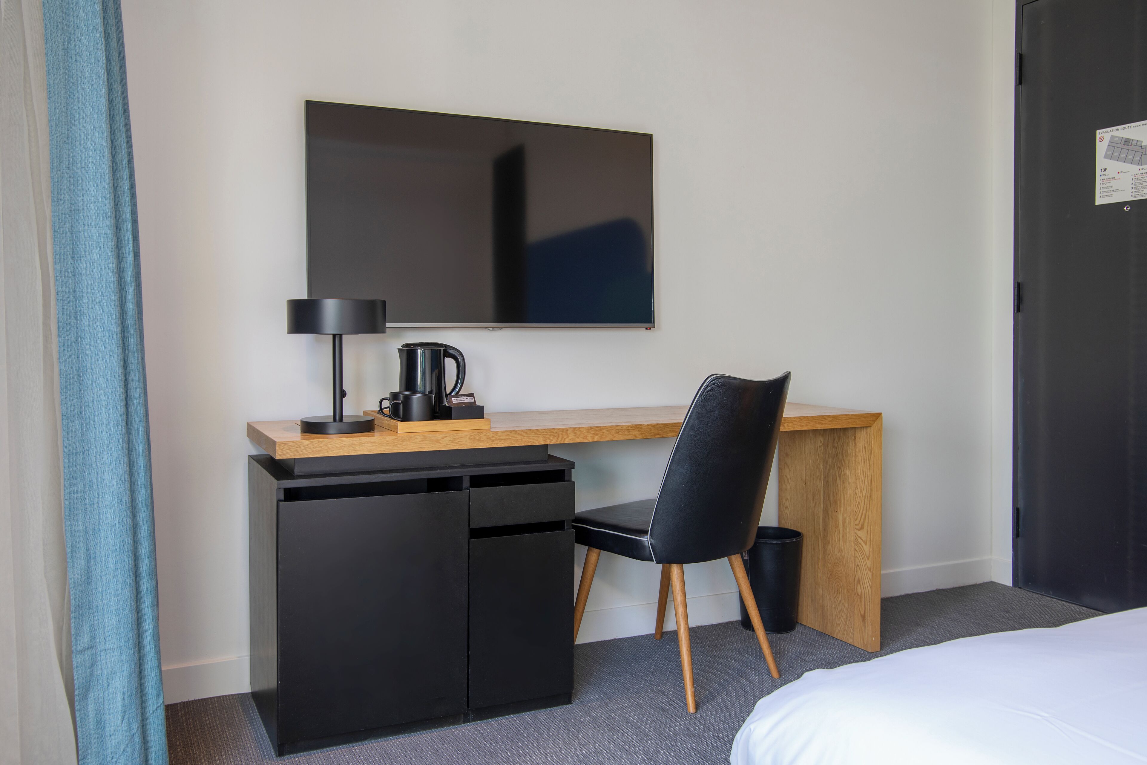 A hotel room with a bed, a desk with a computer, a chair, a lamp, and a coffee maker.