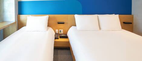 Habitación de hotel con dos camas, cabecera de madera, mesita de noche con teléfono y pañuelos, y una pared decorativa azul.
