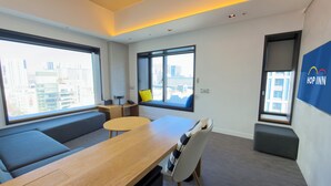 A modern hotel room with a wooden desk, a sofa, a small round table, and a bench. There are large windows offering a city view. - HOP INN Seoul Myeongdong (Seoul)