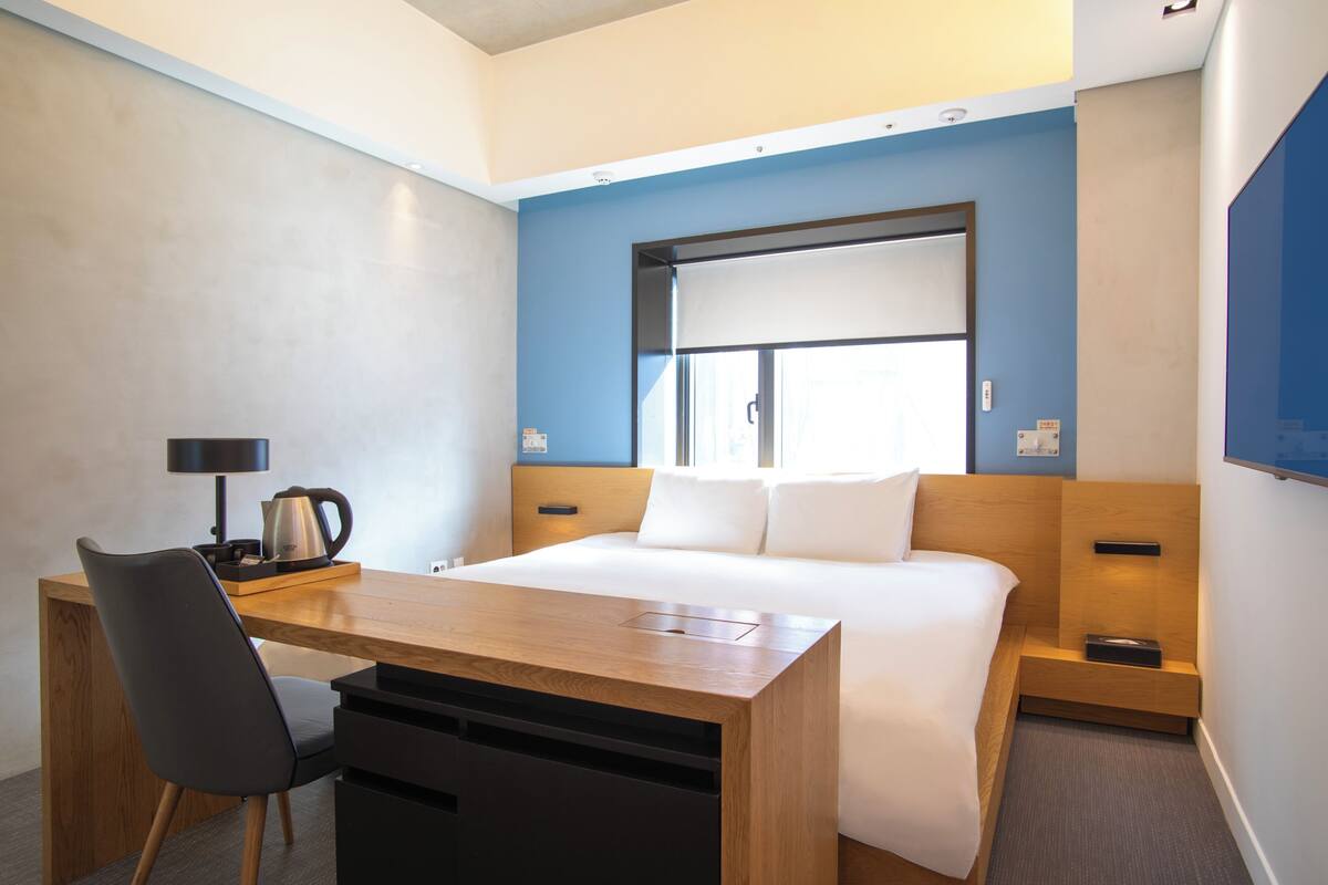 Ein Hotelzimmer mit Bett, Schreibtisch, Stuhl, Kaffeemaschine und Fernseher.
